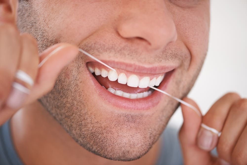 Flossing teeth to remove plaque between teeth and support healthy gums.